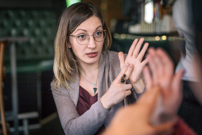 A woman communicates with another woman, who is unrecognizable, using sign language.