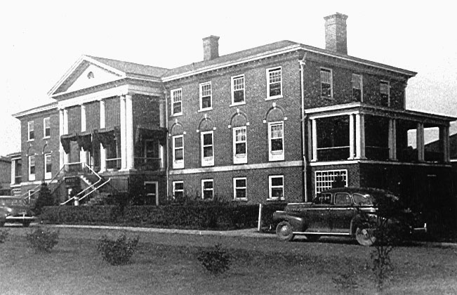 Black-and-white photo from 1943 of a building located in Institute, West Virginia, which used to house DRS' Charleston District offices. It’s a three-story brick building with white columns on the front and a side porch and has two dark cars in front.