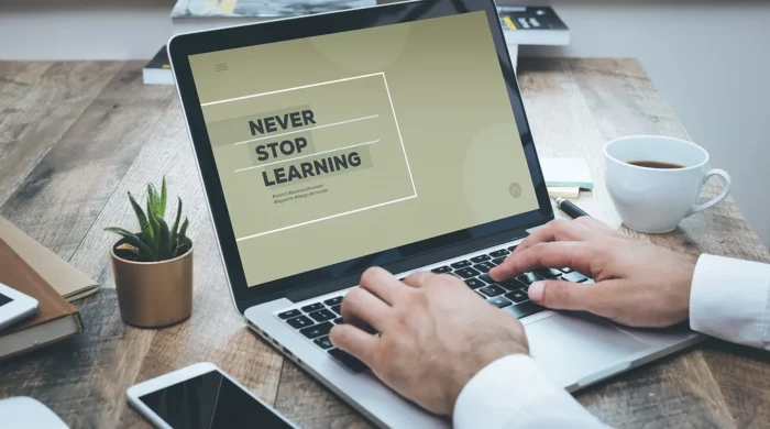 Man's hands typing on a laptop computer. The computer screen depicts the words "never stop learning."